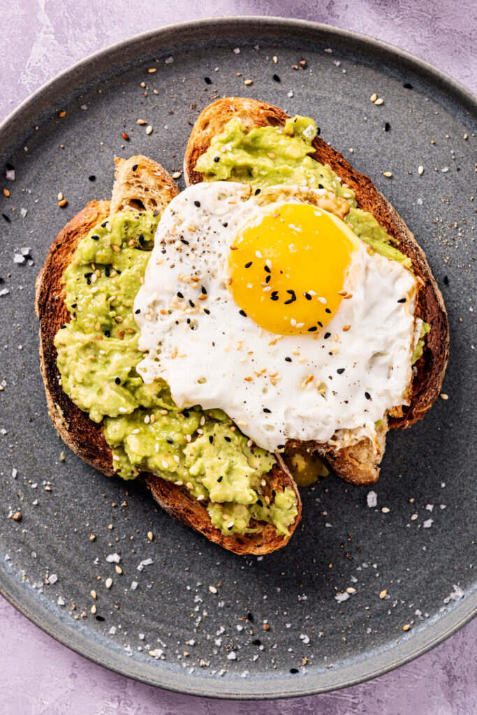 Golden toasted sourdough bread topped with mashed avocado, cherry tomatoes, feta cheese, and microgreens on a rustic wooden board